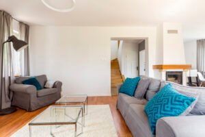 Sala de estar pequeña con muebles grises y azules con escalera de fondo